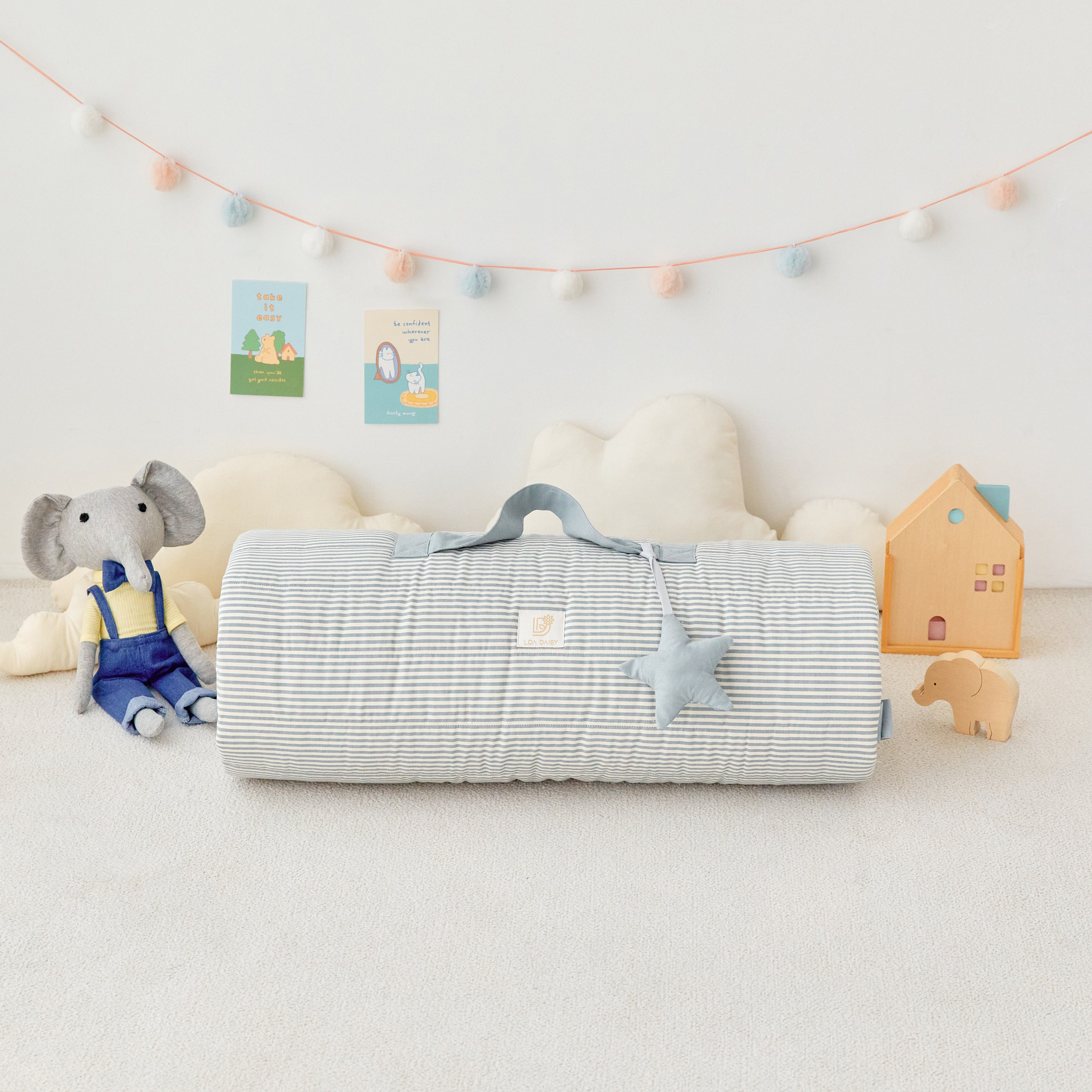 Children's room with a baby bouncer, plush toys, rolled Blue Stripe Portable Nap Mat blanket on a light-colored floor.