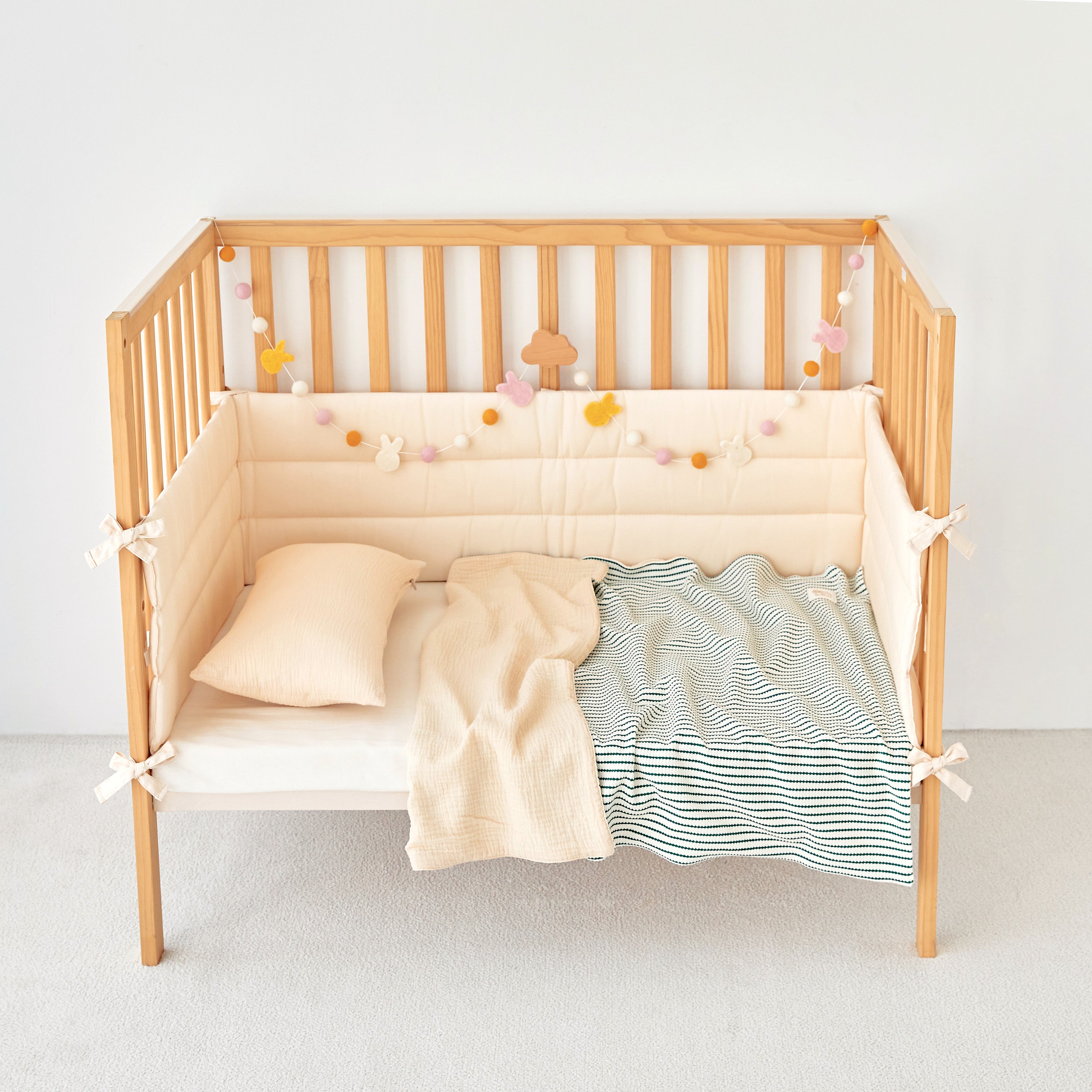 Wooden crib with green striped beige bedding and a striped green knit gauze toddler blanket on a plain background