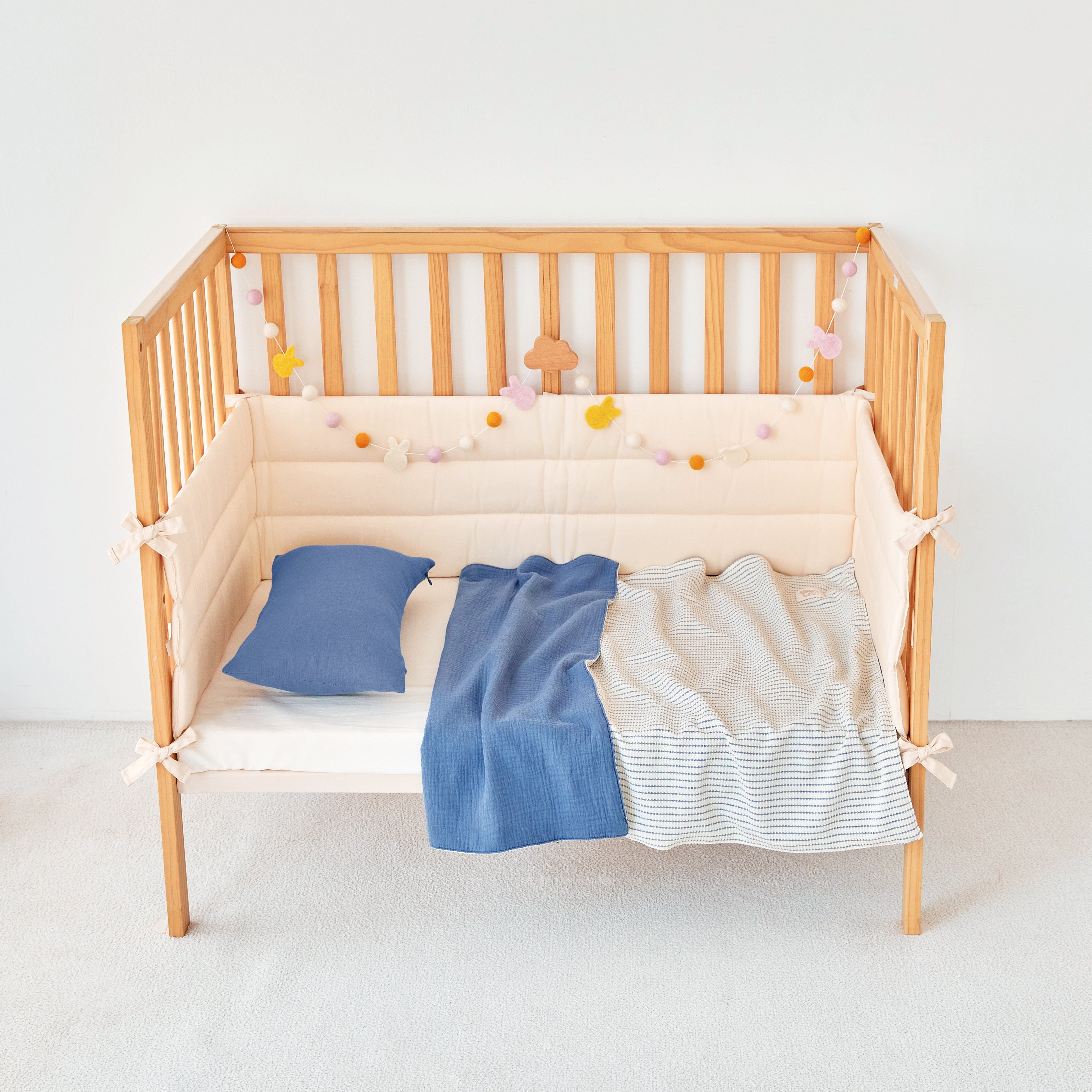 Wooden crib with beige mattress, blue striped knit gauze baby blankets, and decorative items on a white background