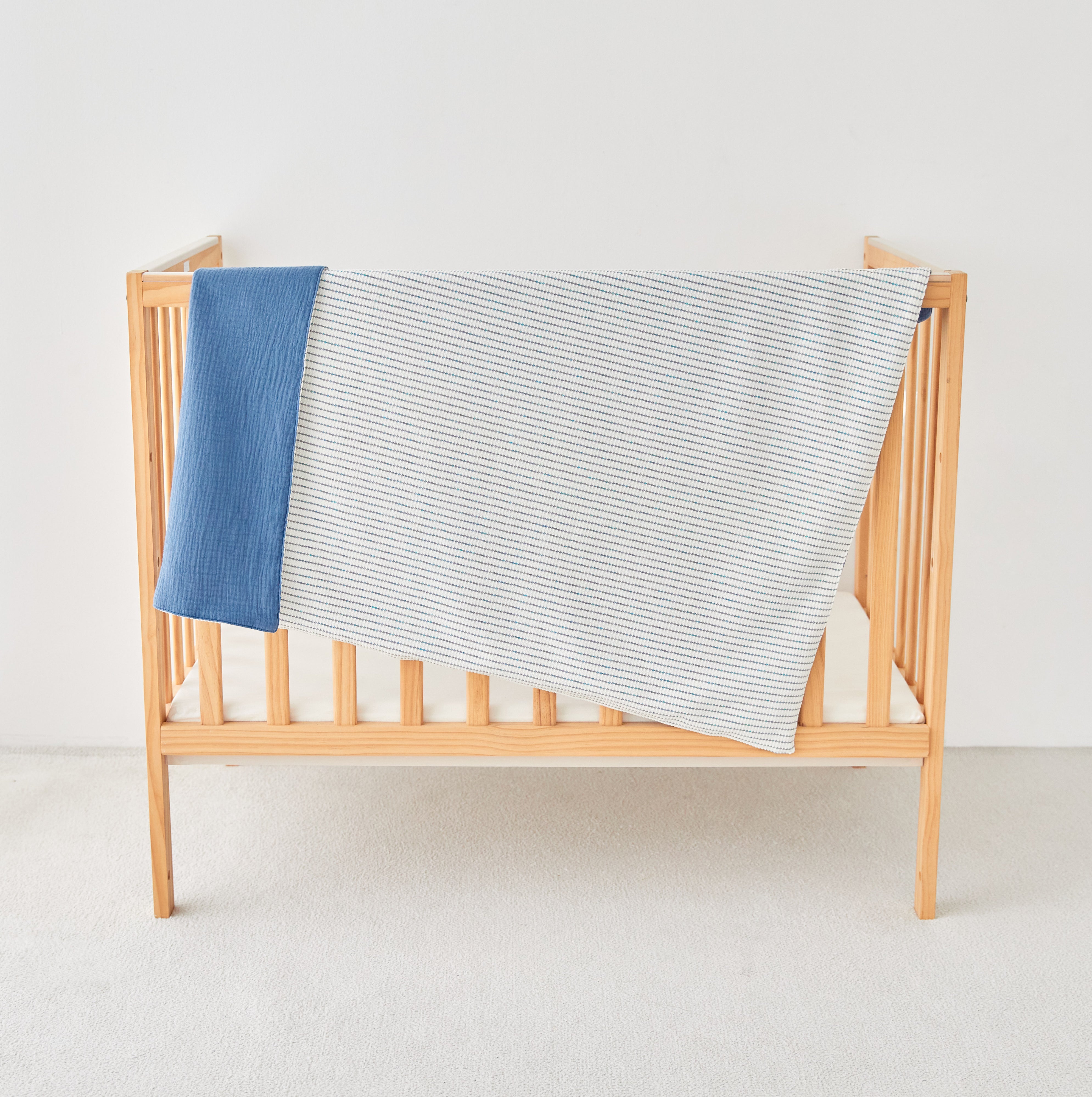 Wooden crib with a blue and white striped toddler knit gauze blanket on a light background