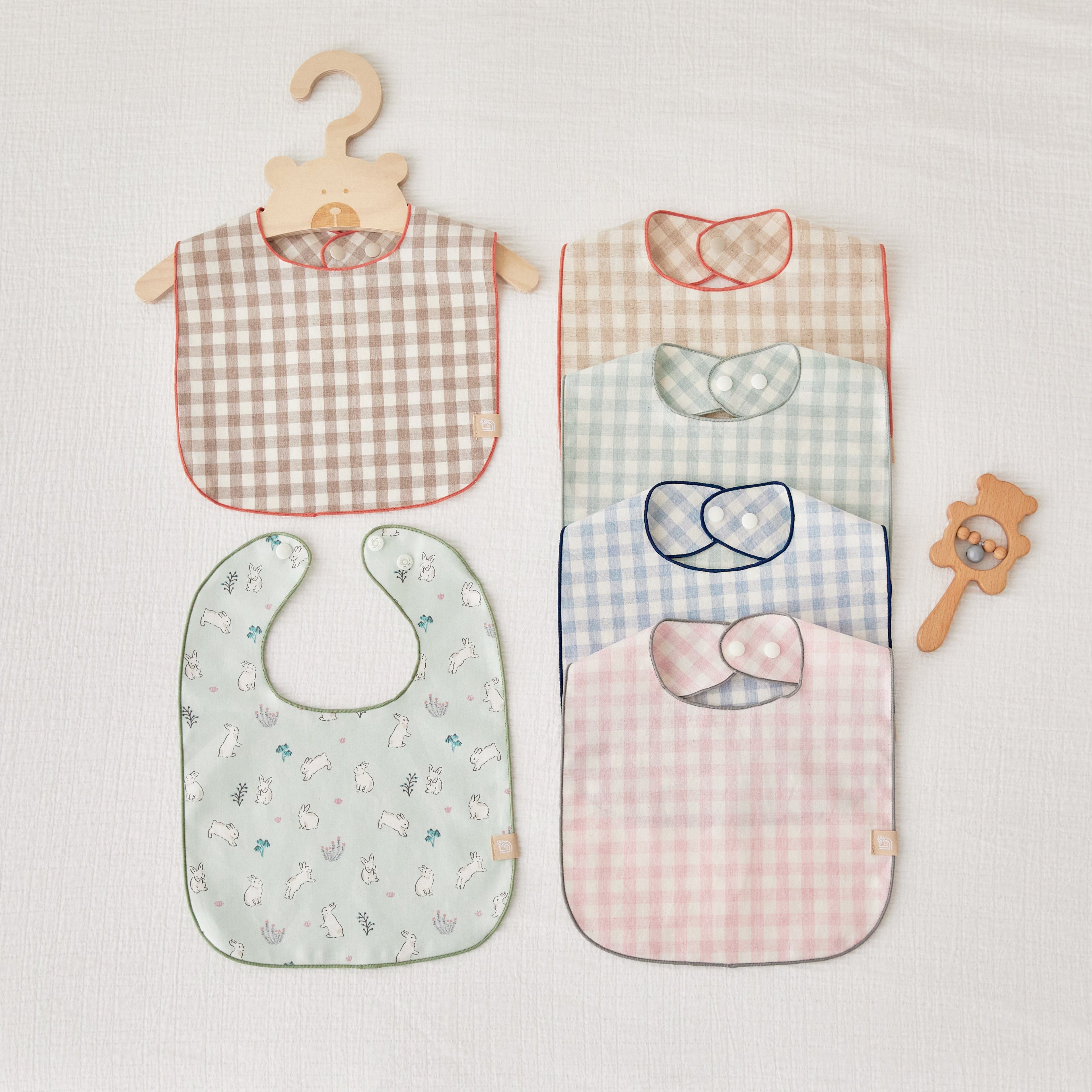 Set of ginham check waterproof baby bibs and a teething ring on a light gray background