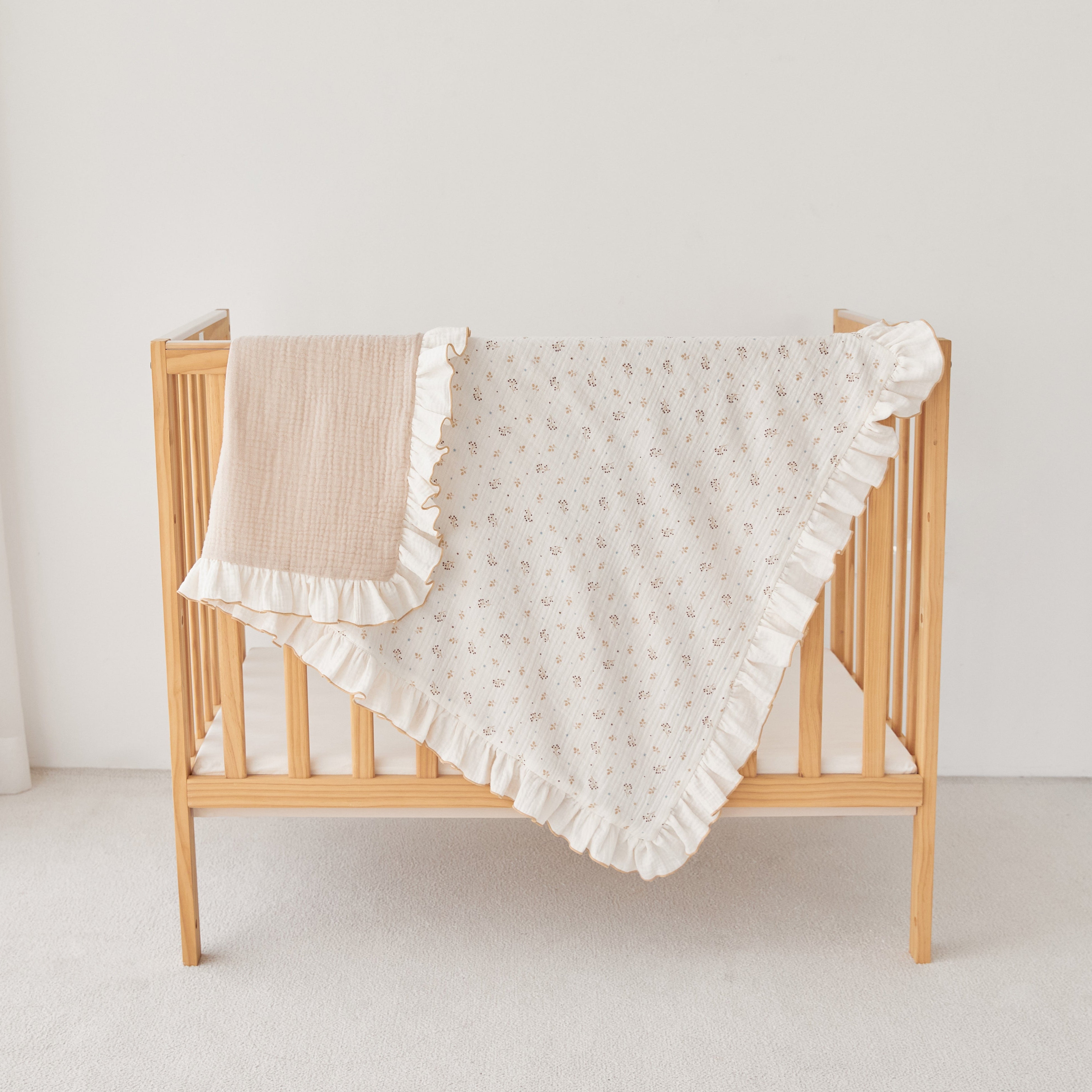 Wooden crib with a beige and ivory ruffled blanket on a light background