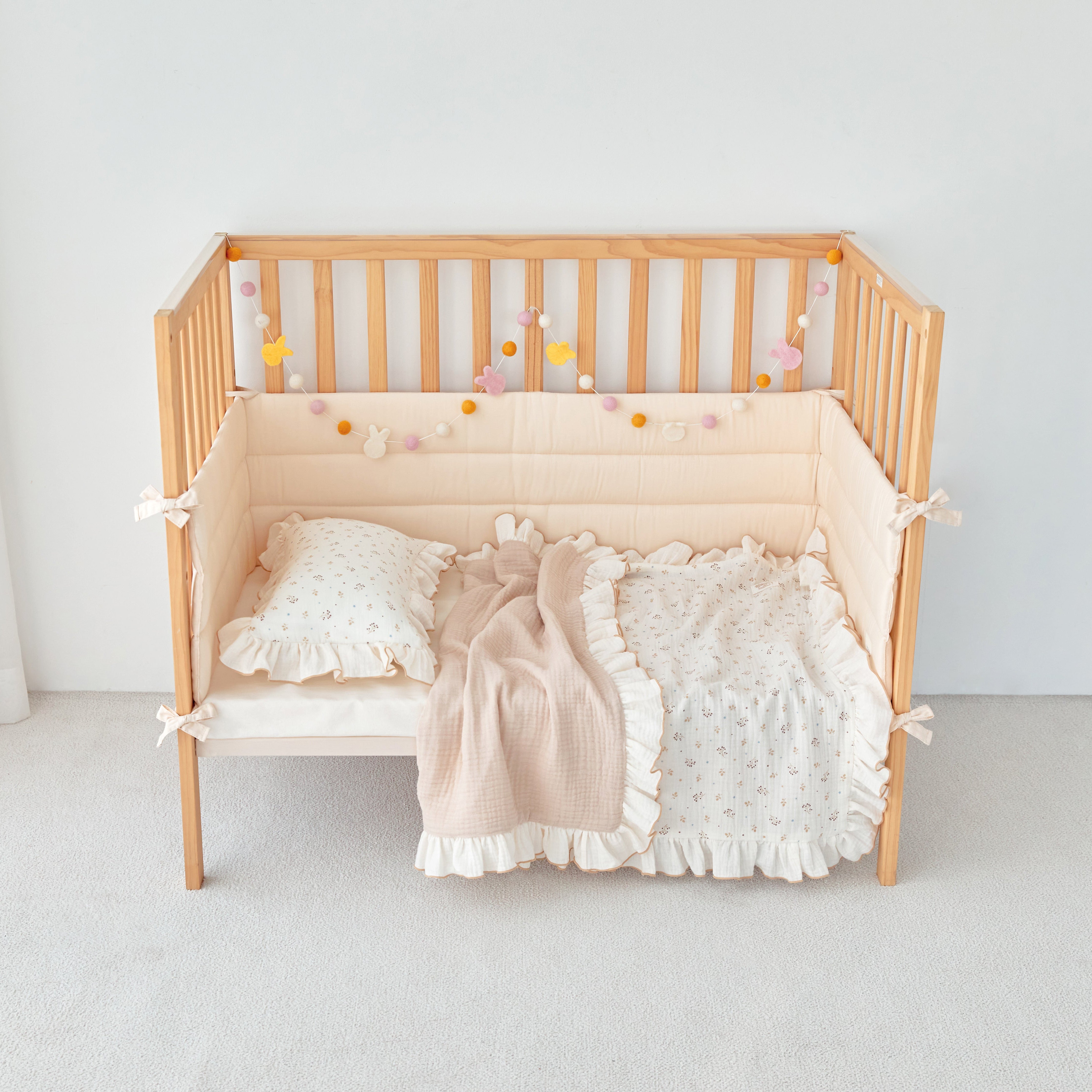 Wooden crib with ivory beige ruffle baby bedding and decorative elements on a plain background