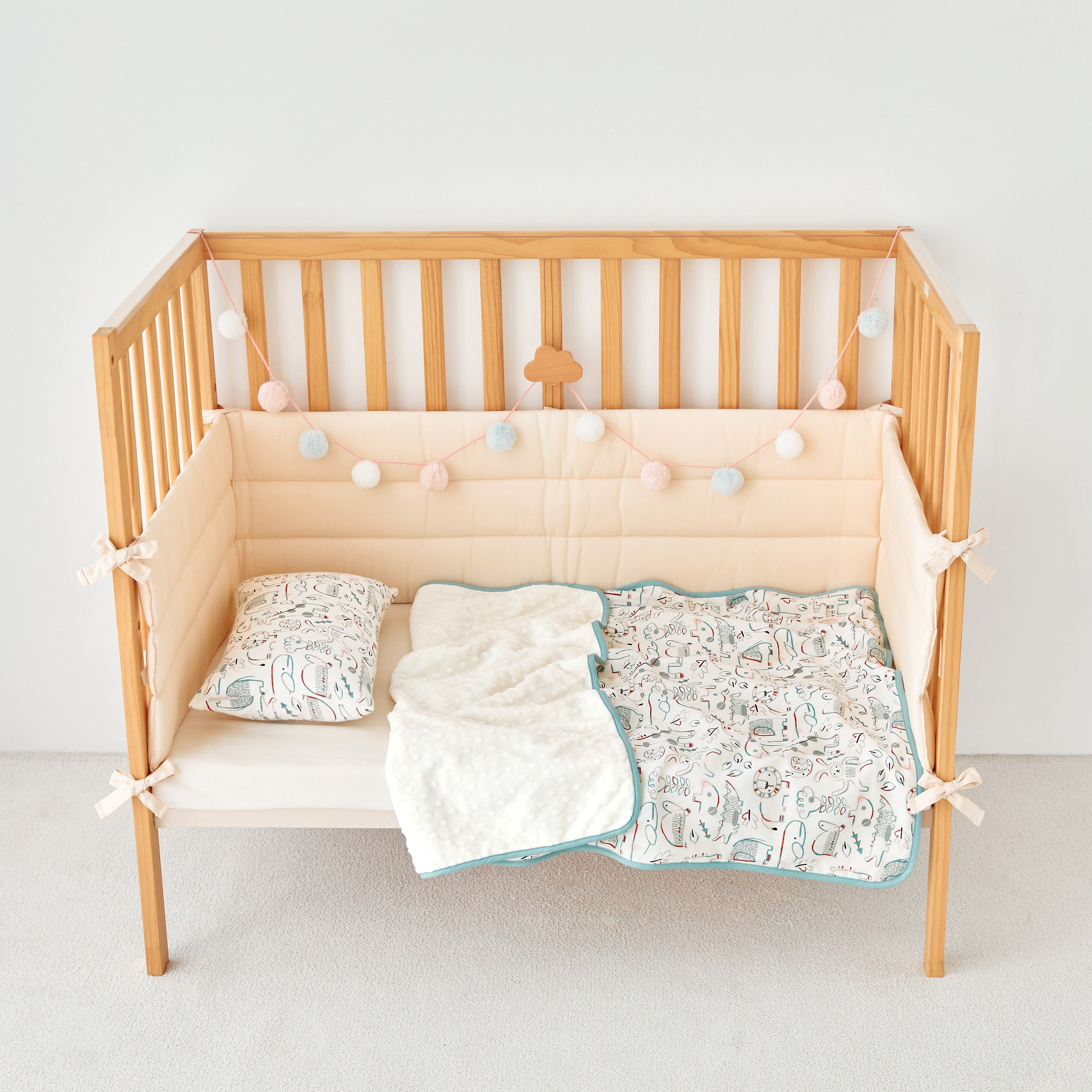Wooden crib with beige bumper pad, white blanket, and baby zoo animal patterned quilt on a light gray floor.