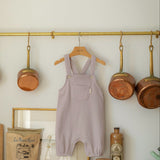 Purple children's overalls hanging on a rack in a kitchen with pots and a framed picture.
