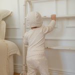 Child in a small floral print outfit standing next to a crib in a nursery.