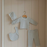 Baby outfit set with pajama long sleeves pants, bib, and hat hanging on a wooden shelf.