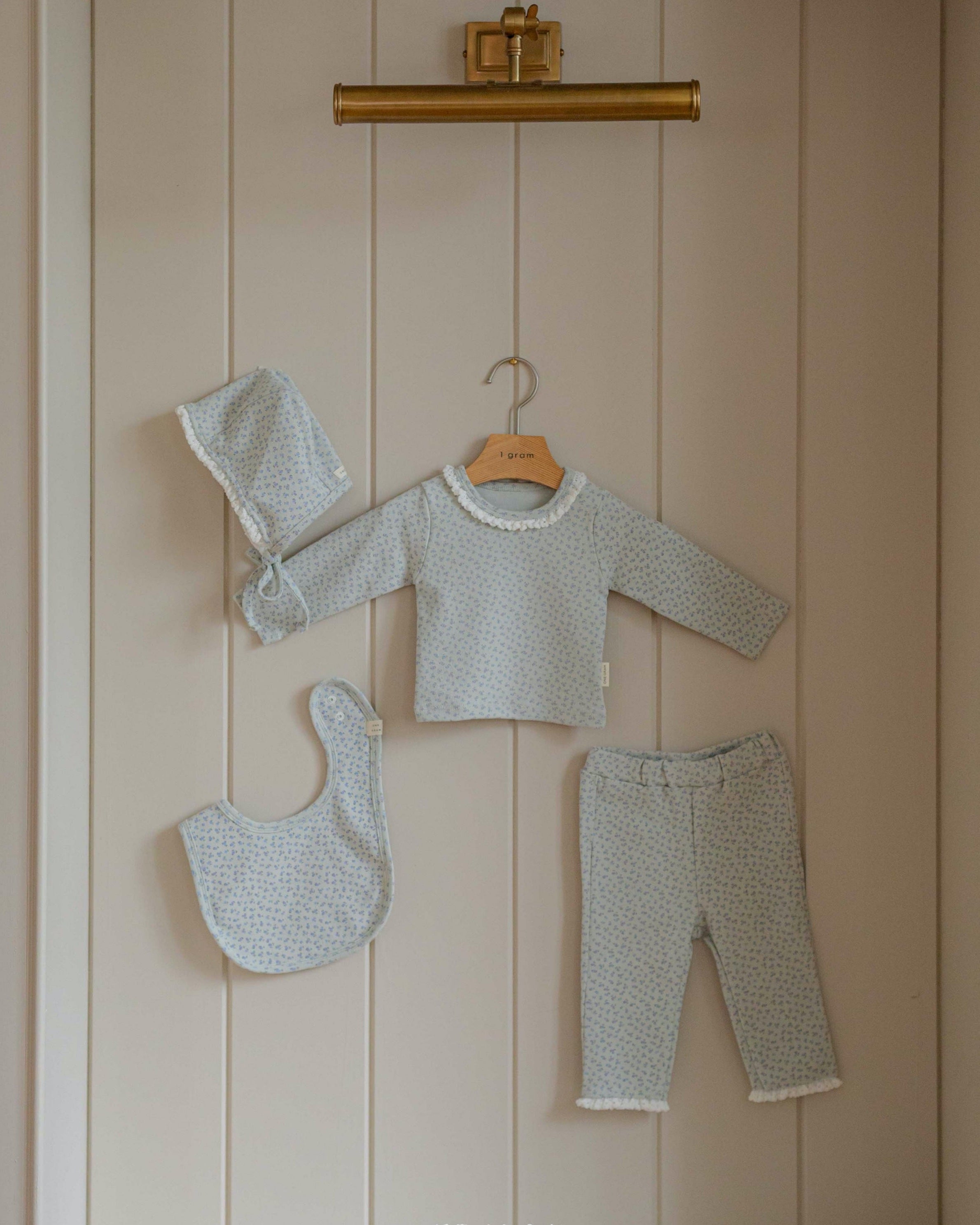 Baby outfit set with pajama long sleeves pants, bib, and hat hanging on a wooden shelf.