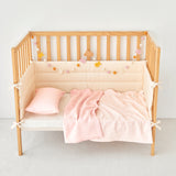 Wooden crib with pink striped knit gauze baby bedding and decorative elements on a white background