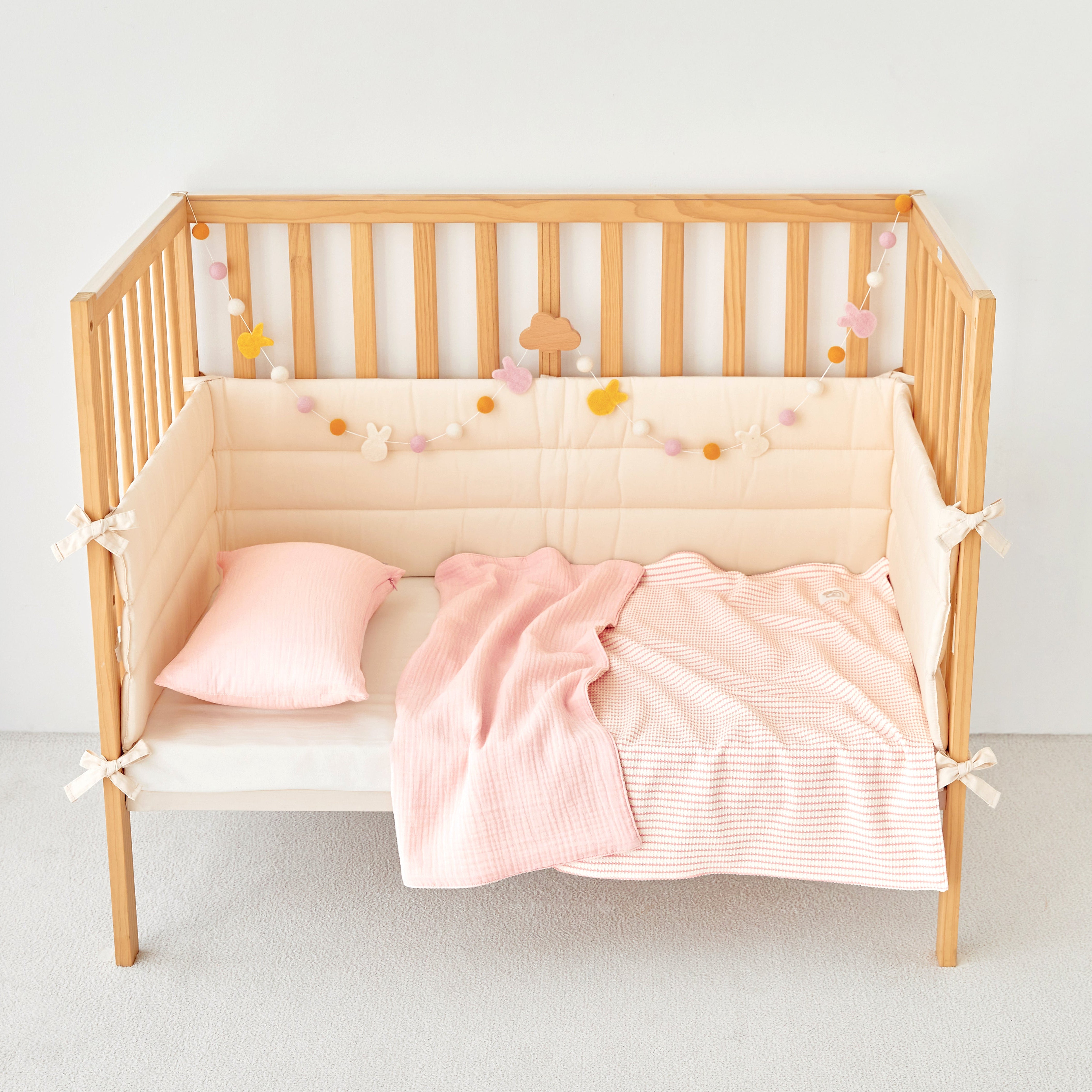 Wooden crib with pink striped knit gauze baby bedding and decorative elements on a white background