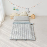 Children's blue striped portable sleeping nap mat with pillow on a light-colored floor, surrounded by toys and decorations.