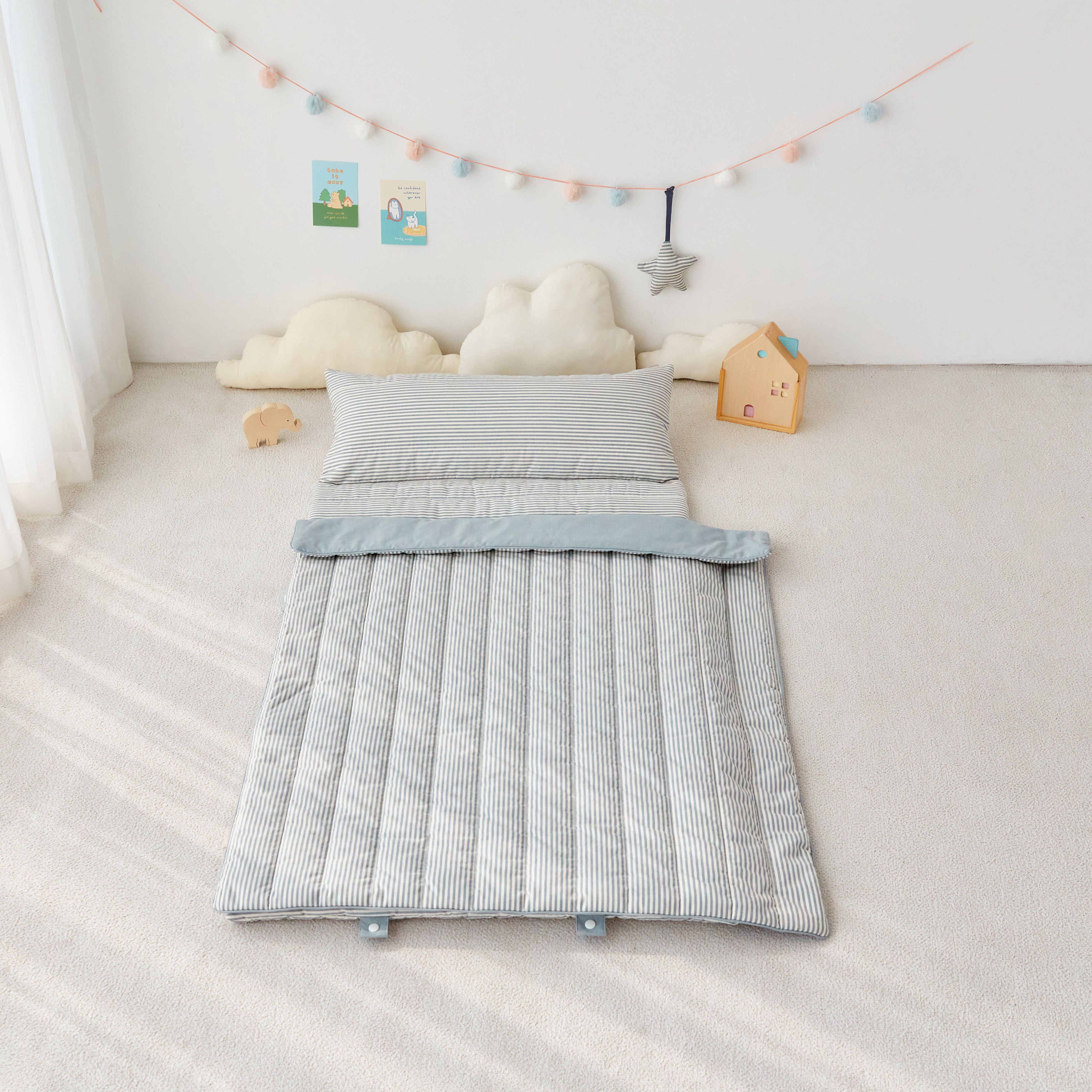 Children's blue striped portable sleeping nap mat with pillow on a light-colored floor, surrounded by toys and decorations.