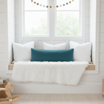 Window seat with white cushions and a slate blue body pillow in a bright nursery room.