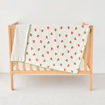 Crib with a cherry-patterned baby toddler blanket on a white background
