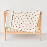 Crib with a cherry-patterned baby toddler blanket on a white background