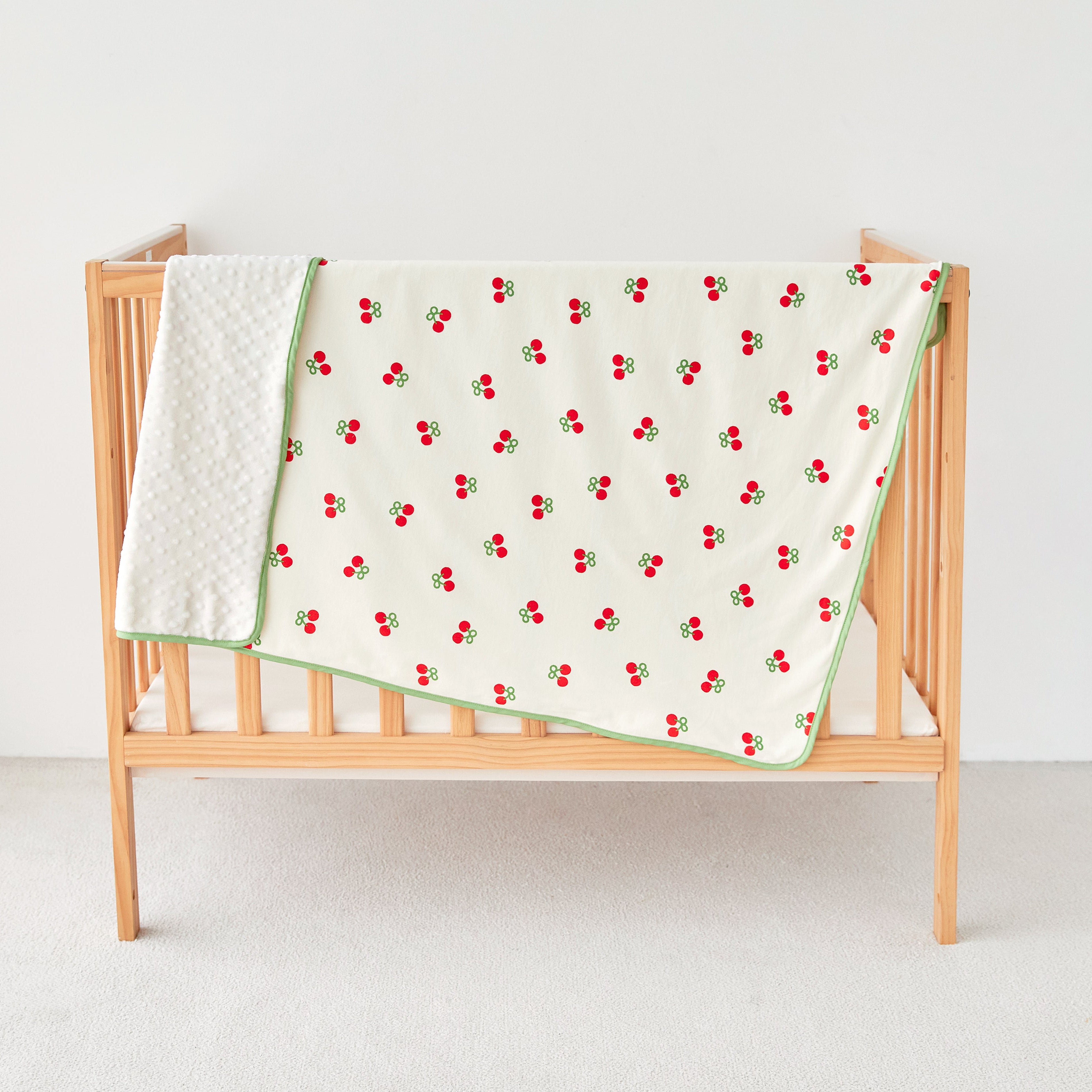 Crib with a cherry-patterned baby toddler blanket on a white background