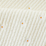 Close-up of a textured white kids nap mat blanket with embroidered daisies 
