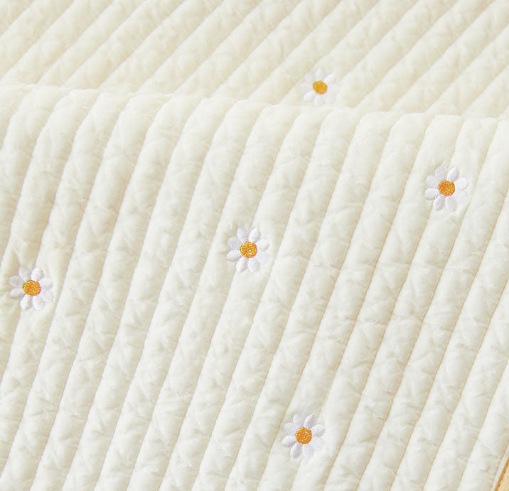 Close-up of a textured white kids nap mat blanket with embroidered daisies 