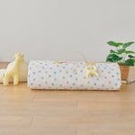 Roll-up portable nap mat blanket with a handle in yellow pink blue bunny rabbit pattern on a wooden floor with toys and a plant