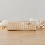 Rolled up gingham brown tan beige checkered baby nap mat blanket with stuffed toy heart name tag on a wooden floor with toys around