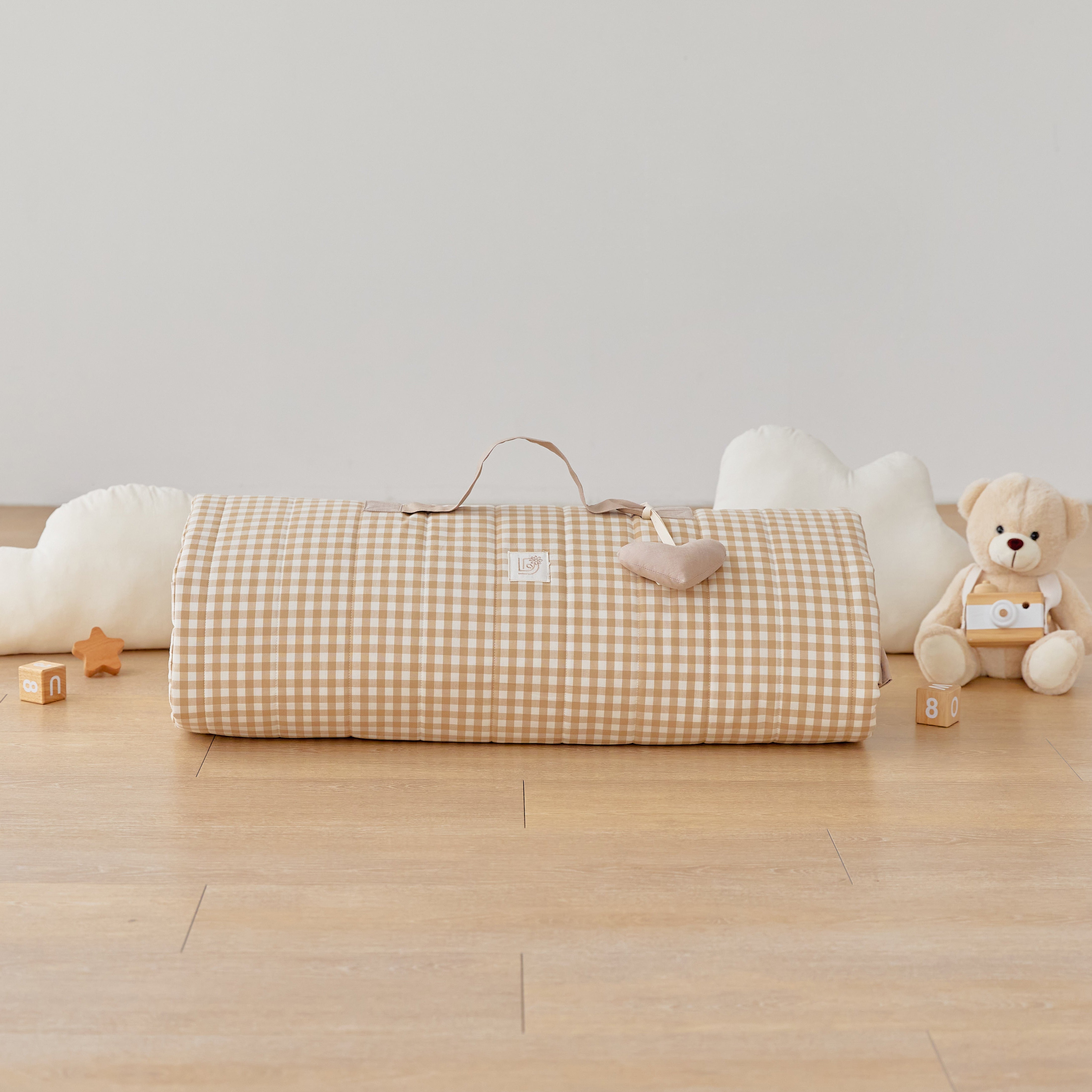 Rolled up gingham brown tan beige checkered baby nap mat blanket with stuffed toy heart name tag on a wooden floor with toys around
