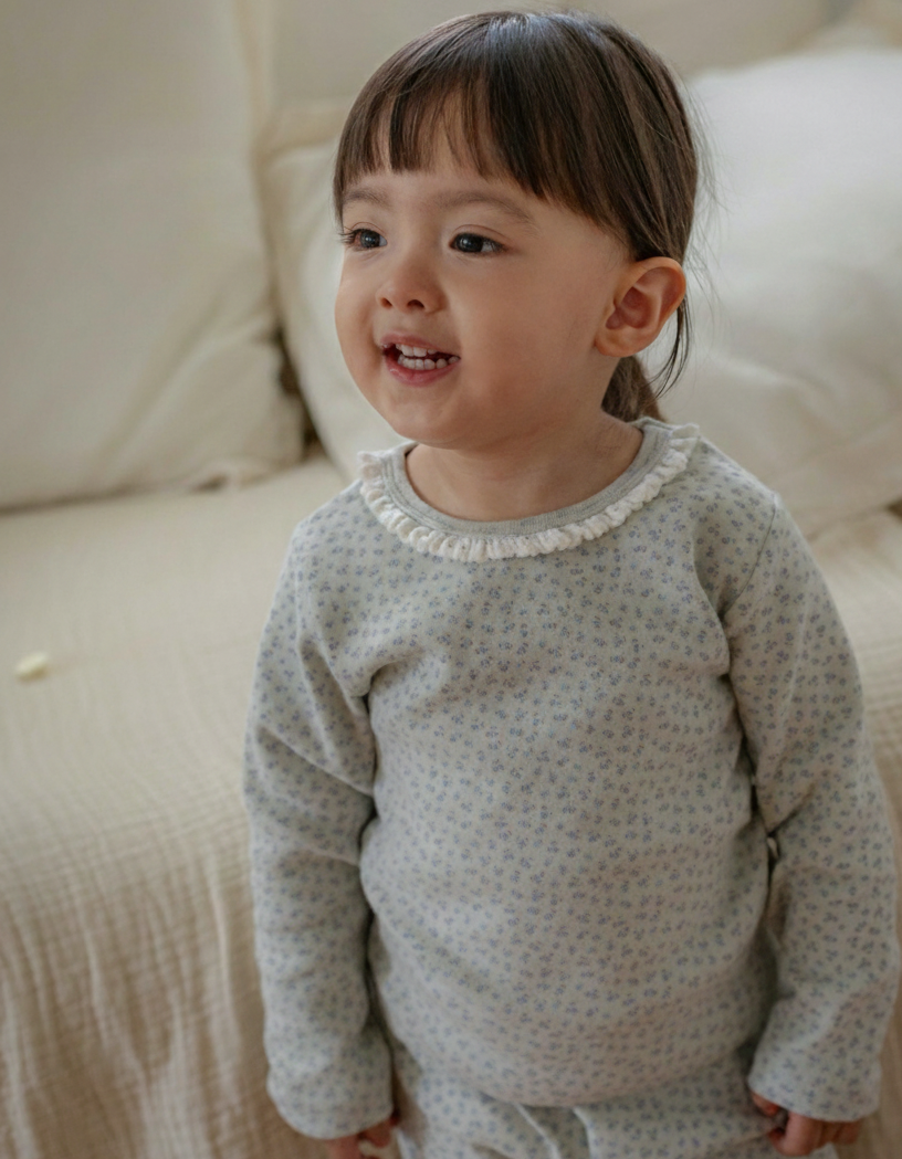 Child wearing a light sky blue outfit with a subtle floral pattern, standing on a beige surface.