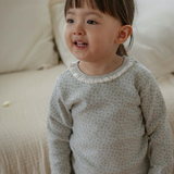 Child wearing a light sky blue outfit with a subtle floral pattern, standing on a beige surface.