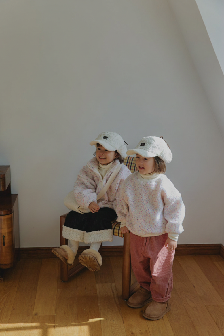 Two children in matching outfits standing on a wooden floor with a plain wall background.