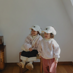 Two children in matching outfits standing on a wooden floor with a plain wall background.
