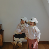 Two children in matching outfits standing on a wooden floor with a plain wall background.