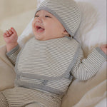 Baby in a gray white striped onesie outfit and hat lying on a soft surface