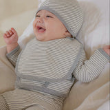 Baby in a gray white striped onesie outfit and hat lying on a soft surface