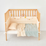 Wooden crib with green striped beige bedding and a striped green knit gauze toddler blanket on a plain background