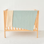 Wooden baby crib with a green and white striped knitted gauze blanket draped over it on a white background