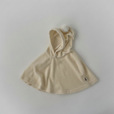 Beige baby cape dress with pompom attached hood on a light gray background