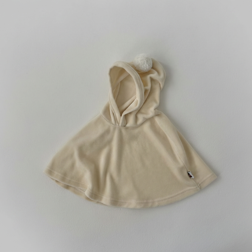 Beige baby cape dress with pompom attached hood on a light gray background