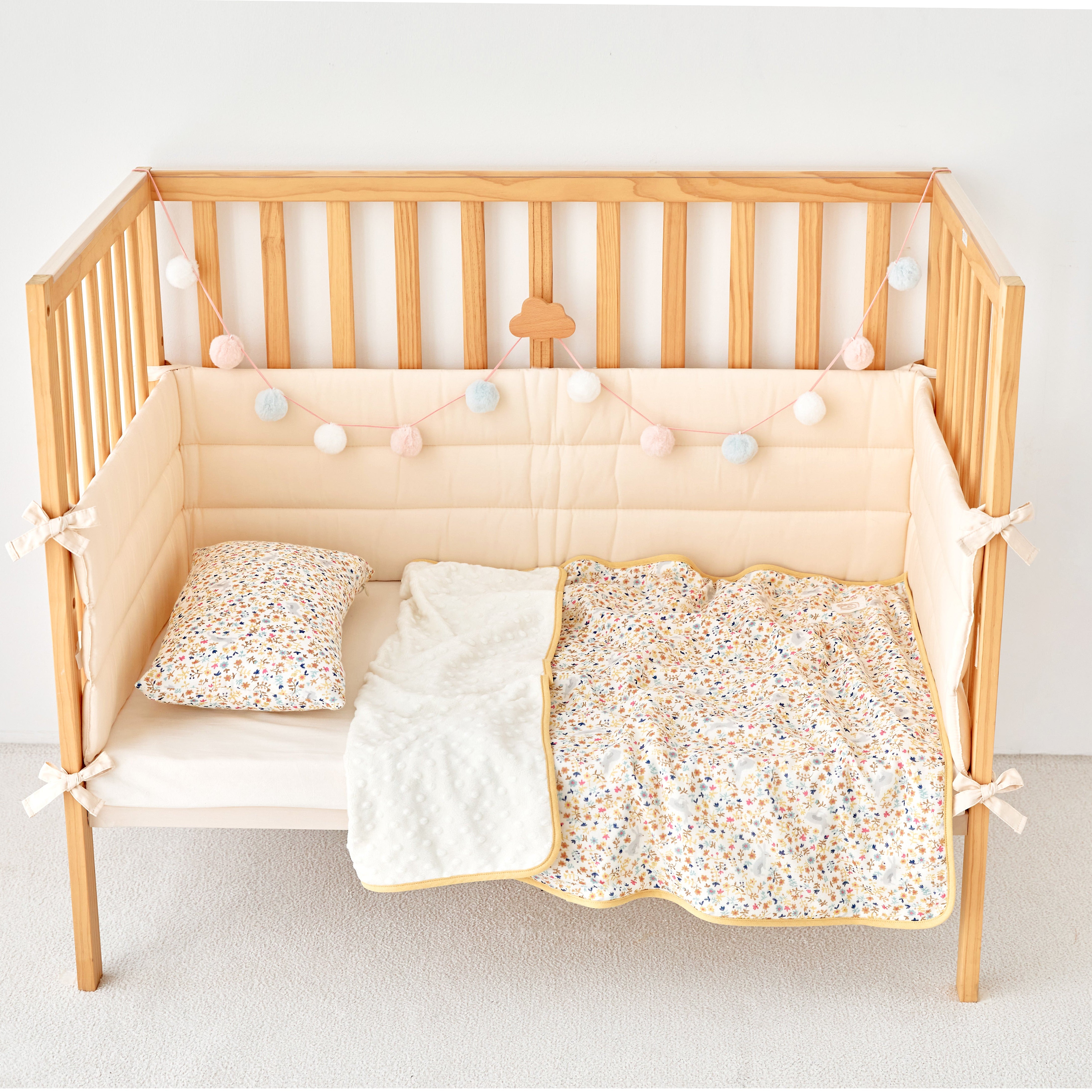 Wooden crib with beige mattress, floral pillow, and floral rabbit mustard baby blanket on a white background