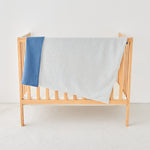 Wooden crib with a blue and white striped toddler knit gauze blanket on a light background