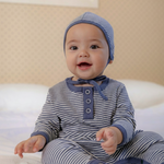 Baby boy wearing a navy blue white striped outfit and hat on a bed