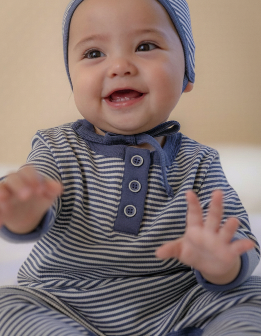 Baby wearing a blue and white striped outfit with a matching hat, sitting on a beige surface.