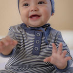 Baby wearing a blue and white striped outfit with a matching hat, sitting on a beige surface.