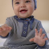 Baby wearing a blue and white striped outfit with a matching hat, sitting on a beige surface.