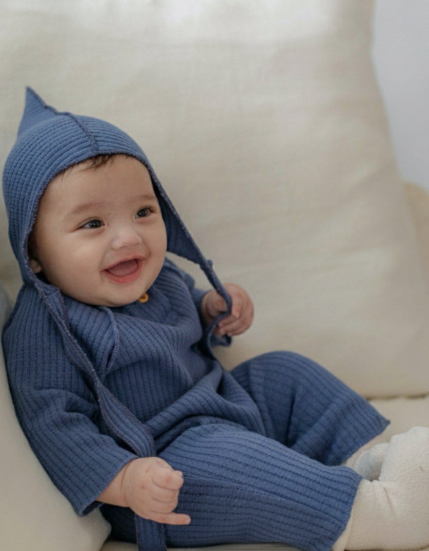 Baby wearing a blue knitted outfit with a matching bonnet on a white background
