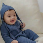 Baby wearing a blue knitted outfit with a matching bonnet on a white background