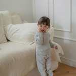 Child in floral printed pajama standing in a room with a white couch and wooden floor.