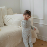 Child in floral printed pajama standing in a room with a white couch and wooden floor.