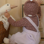 Child in a violet romper, brown outfit with white polka dots playing with a toy goose in a room.