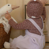 Child in a violet romper, brown outfit with white polka dots playing with a toy goose in a room.