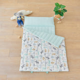 Children's quilt portable nap mat blanket with animal pattern on a wooden floor with toys and a plant.