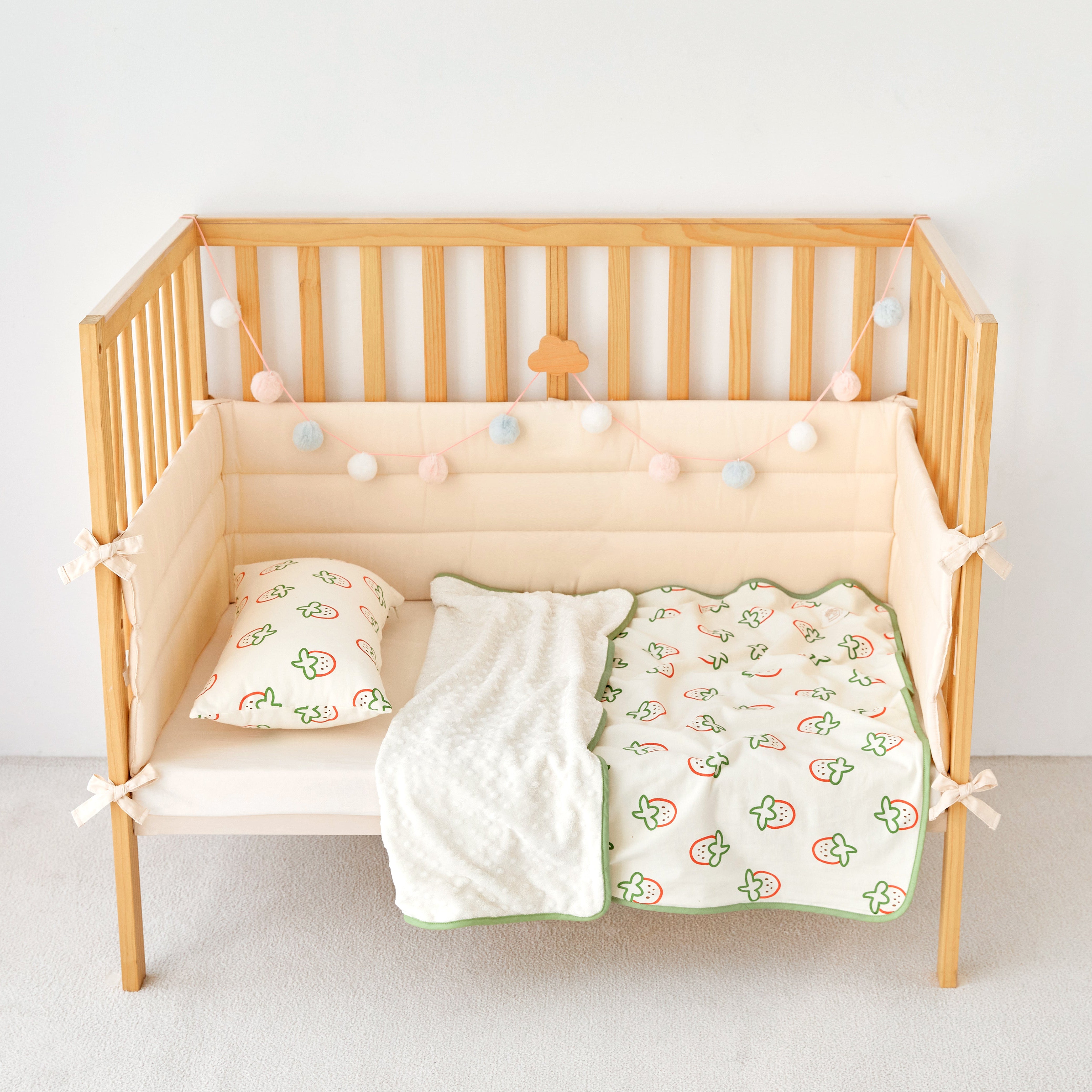 Wooden crib with strawberry print knitted cotton and minky baby blanket including a white blanket and green crib sheet with patterns on a plain background